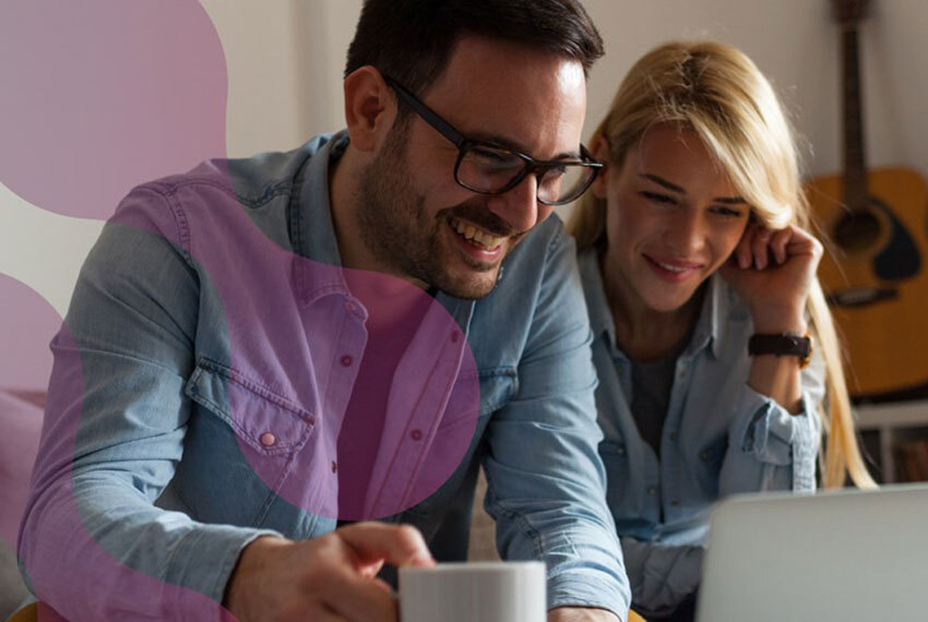 Man and Woman in Denim Shirts Smiling at Laptop Screen While Drinking Coffee