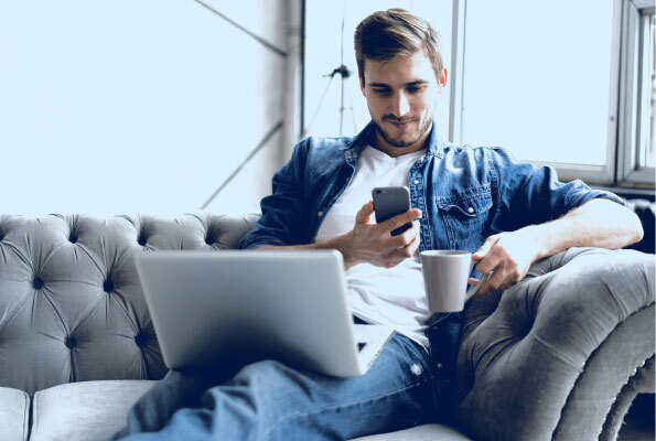 Man on Couch Enjoying Coffee with Smart Phone and Laptop