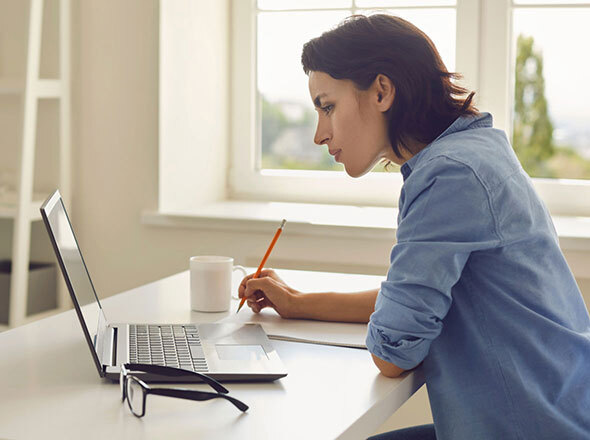 Woman Writing and Looking at Laptop