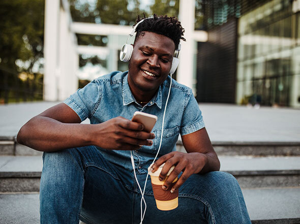 Man Looking at Smart Phone with Coffee and Headphones on