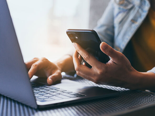 Left Hand Holds iPhone while Right Hand Types on Laptop