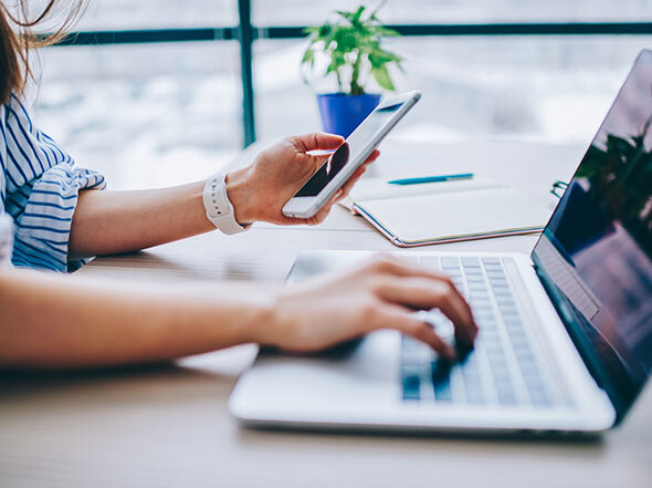 Left Hand Holds iPhone while Right Hand Types on Laptop