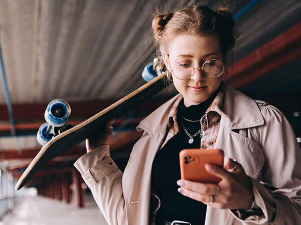 Stylish Girl Looking at Smart Phone While Holding Skateboard
