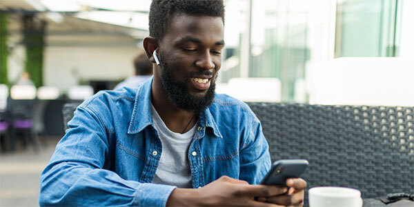 Man in Denim Shirt at Cafe Wearing Air buds and Using Cell Phone