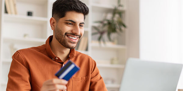 Man in Orange Button Down Shirt Smiling While Using Credit Card to Pay Bill Online