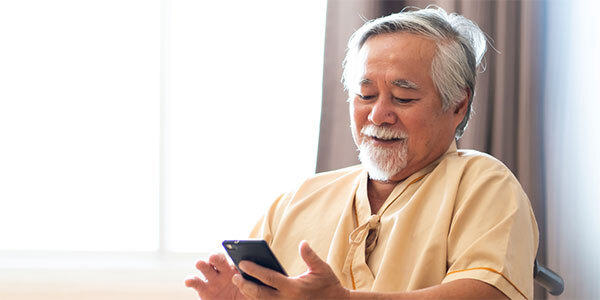 Older Man in Hospital Scrubs Using Cellphone in Wheelchair