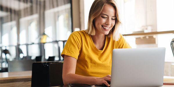 Woman in Yellow T-Shirt Smiling at Office Laptop